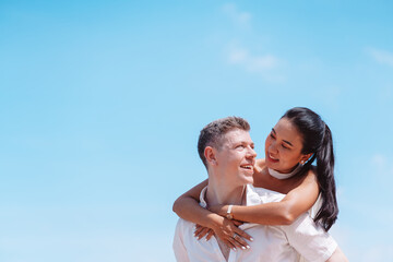 Young couple in love outdoor. Happy man giving piggyback ride to his woman and laughing at tropical beach. Girlfriend getting piggyback ride from boyfriend at sunrise in summer.