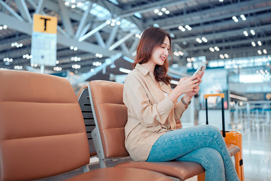 Happy asian tourist woman passenger using mobile smartphone with suitcase traveling between waits for flight in Airport Terminal, Browse Internet, flight check in, Tourist journey trip concept