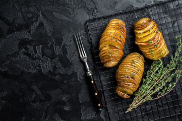 American traditional Homemade Hasselback Potato with Fresh Herbs. Black background. Top view. Copy...