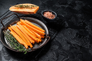Sliced Sweet potatoes in a steel tray, fresh batata fries ready for cooking. Black background. Top view. Copy space