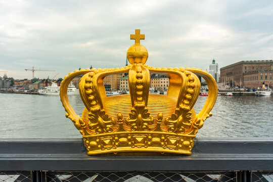 Golden crown decoration on the railing of a public footbridge with city Stockholm in the background.