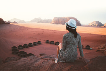Woman tourist in dress sit on cliff at viewpoint on sunset in Wadi Rum desert - valley Wadi Saabit. Jordan explore concept - obrazy, fototapety, plakaty