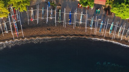 Aerial top view of beautiful bay on ocean shore with white Jukung fishing boats and tropical green. Sea waves rolling on quiet beach with bali local fishery vehicles. Drone view of seaside. Soft focus