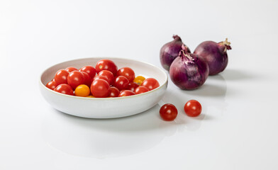 Small tomatoes in a white bowl with red onions