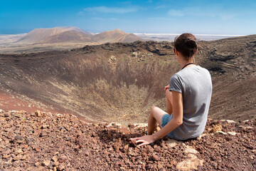 A woman looking at the volcano's crater and distant mountains enjoying her vacation and beautiful weather (Volcano Calderon Hondo - Fuerteventura, Canary Islands)