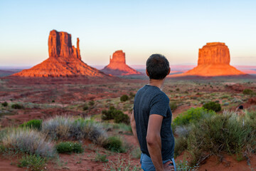 One man tourist standing looking at view of famous buttes in Monument Valley at sunset colorful...