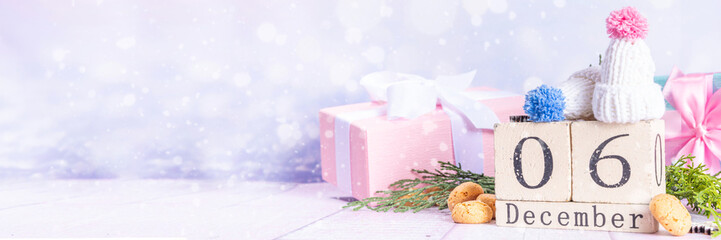 Sinterklaas, Saint Nicholas day background. Kids winter hats, block calendar with December 6 date, pepernoten, candy. Dutch Christmas holiday greeting card on snowy wooden background copy space