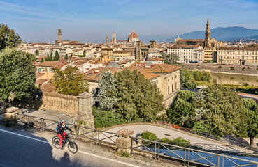 cheerful senior woman cycling with her electric mountain bike above downtown of Florence with stunning view over the old city, Tuscany, Italy