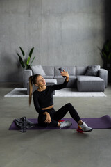 Young smiling sporty athletic fitness trainer instructor woman doing exercises do selfie on mobile cell phone sit on mat floor at home