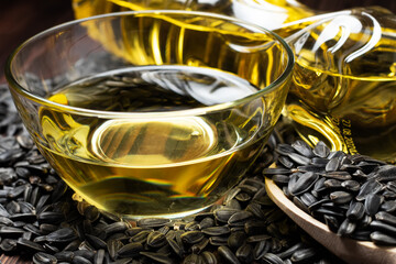 Sunflower oil in glass bowl and bottle with seed in wooden spoon on wooden background