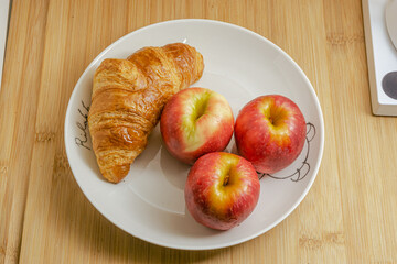 Croissant with apple on white plate and wooden background