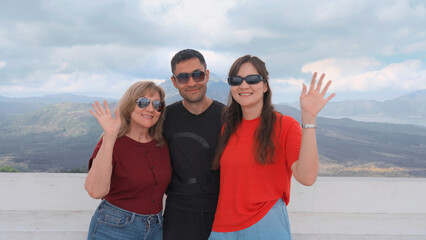 Happy family smiling and waving to camera against beautiful Mountain View. Tourists posing in front of valley and cloud sky during summer vacation trip Group of asian European people. Soft focus