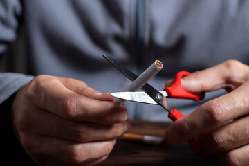 The concept of the fight against smoking and nicotine addiction. A man cuts a cigarette with...