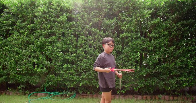 happy cute young Asian children boy enjoy smiling playing bubble soap toy swing on the air with fun against green nature garden on backyard in slow motion, outdoors summer leisure recreation childhood