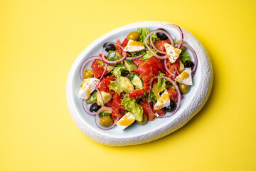Greek salad in a plate on a yellow background