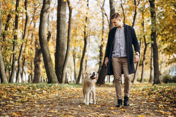 Naklejka na ściany i meble Man with his dog walking in autumn park