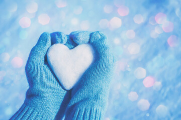 Female hands in knitted gloves with heart of snow in winter day. Love concept. Valentine day...
