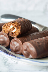 Individual chocolate sponge rolls on a patterned blue and white dish with a serving knife. On a white marble background