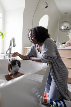 Mother washing hair of son in bathtub in bathroom at home