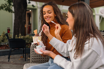 Two girls are having fun and eating delicious ice-cream in the cafe garden on a sunny day.