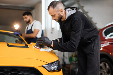 Auto detailing service, polishing of the car. Team of young men workers polishing yellow car body...