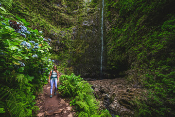 Beautiful athletic woman walks along flowery and farny trail at amazing jungle water fall. Levada...