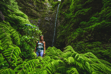 Beautiful athletic woman walks along flowery and farny trail at amazing jungle water fall. Levada...