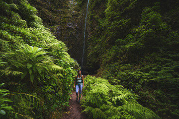Beautiful athletic woman walks along flowery and farny trail at amazing jungle water fall. Levada...