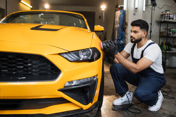 Car detailing and polishing concept. Professional young male car service worker in uniform, holding...