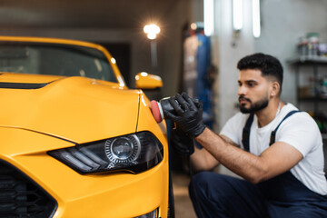 Young handsome bearded man, worker of auto detailing service, holds orbital polisher in the hand...