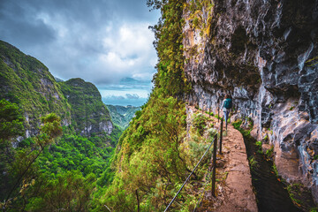 Athletic woman walks at adventurous cliff jungle path along canal. Levada of Caldeirão Verde,...