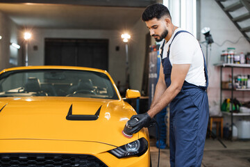 Full length portrait of young handsome man, worker of auto detailing service, holds orbital...