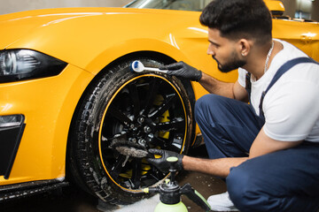 Car washing and detailing workshop. Bearded man worker in protective overalls and rubber gloves,...