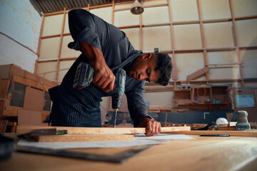 Young man using drill on wood during work at woodworking factory