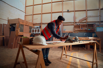 Young man writing with digitized pen on digital tablet on a-frame table in woodworking factory