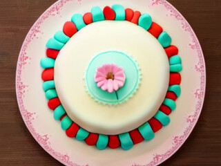 Cake with white fondant, a light pink daisy in the center, green and red accents on a light pink...
