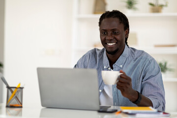 Distance Work. Happy Black Freelancer Guy Drinking Coffee And Using Laptop