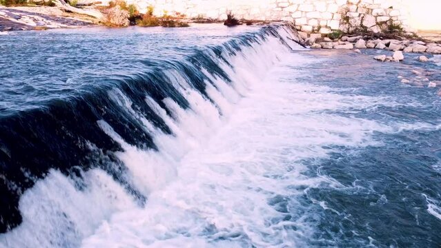 Aerial slow motion shot of a waterfall, Adda river, drone flying over the river at sunset. 