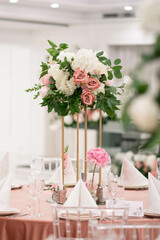 Centerpiece made of green leaves and fresh flowers stands on the dinner table. Wedding day. Fresh flowers decorations. Peony arrangements.