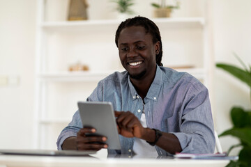 Modern Technologies. Cheerful Young Black Man Using Digital Tablet At Home