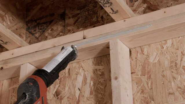 Caulk gun sealing crease between 2x4 wooden studs in wall in slow motion