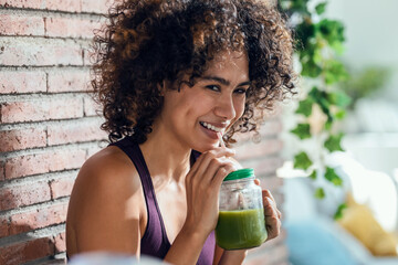 Happy woman drinking a healthy green smoothie standing in the living room at home.