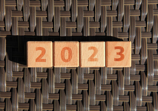 Inscription 2023. Wooden square cubes and numbers on plastic wicker surface means coming New Year Eve. Christmas, holidays and celebration concept. New Year of 2023, year of the black water rabbit