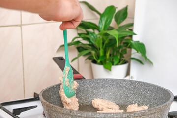 The process of cooking chopped chicken cutlets in a frying pan. Chopped chicken fillet. A portion of meat puree on a silicone shovel. A man is frying chicken cutlets in a frying pan.