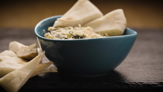 Baked spinach and artichoke dip in small teal colored bowl garnished with triangle slices of pita bread