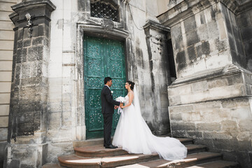 Wedding photo shooting. Bride and bridegroom walking in the city. Married couple embracing and looking at each other. Holding bouquet