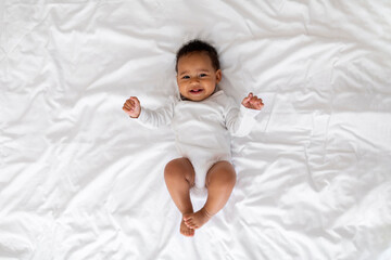 Portrait Of Cute Laughing Black Infant Baby Lying On Bed At Home