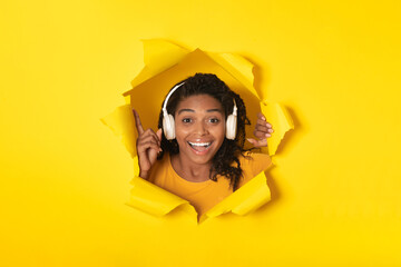 Black Woman Wearing Headphones Looking Through Hole In Yellow Paper
