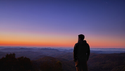 a man, traveller enjoys the majestic view on mountains in morning light, welcoming a new day