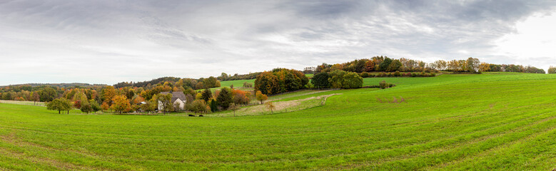 Fototapeta na wymiar Farm house in the middle of a huge green field. Panoramic rural autumn landscape in North Rhine Westphalia in Germany.